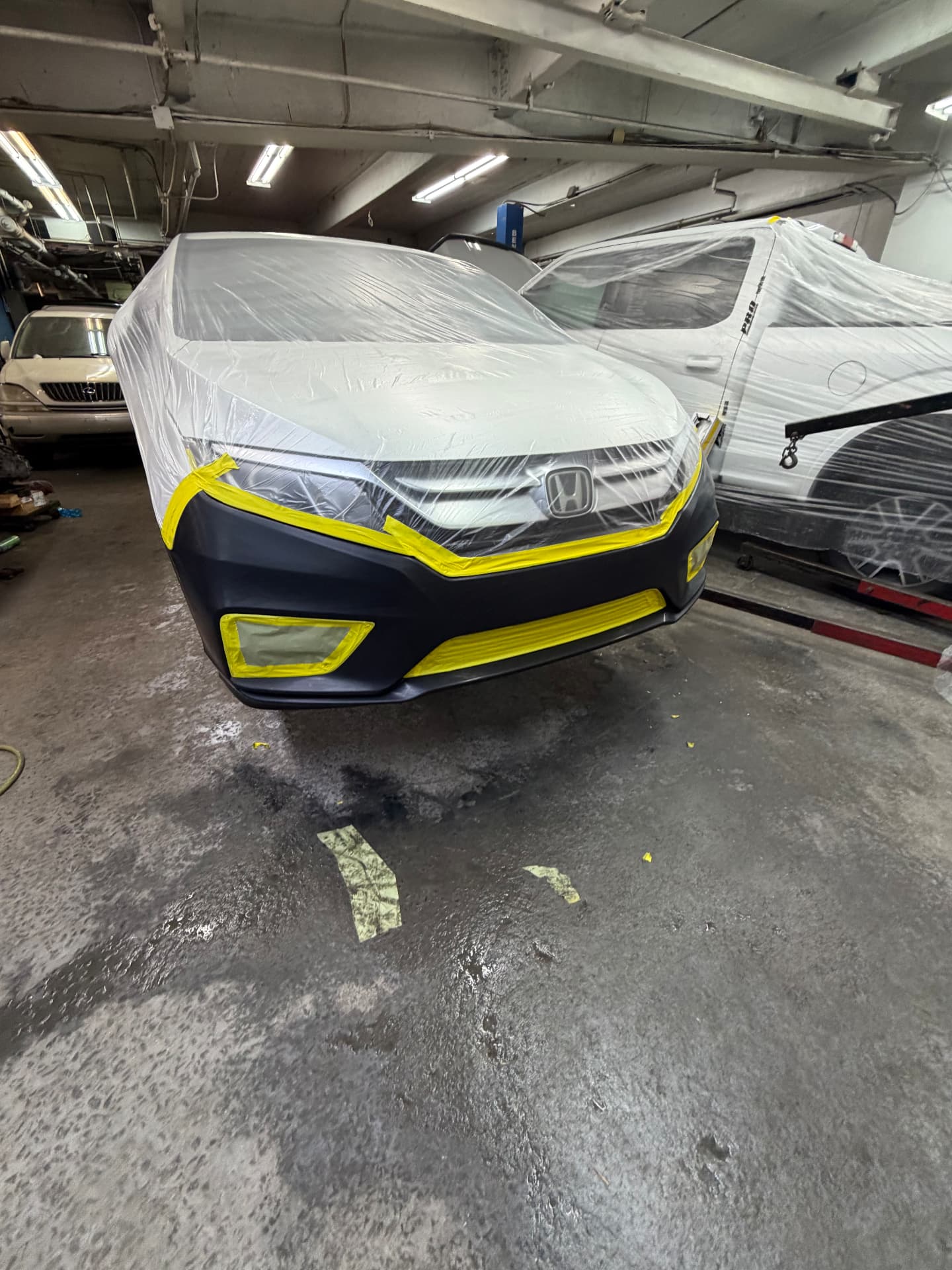 Honda sedan masked in plastic and tape with the front bumper primed for paint